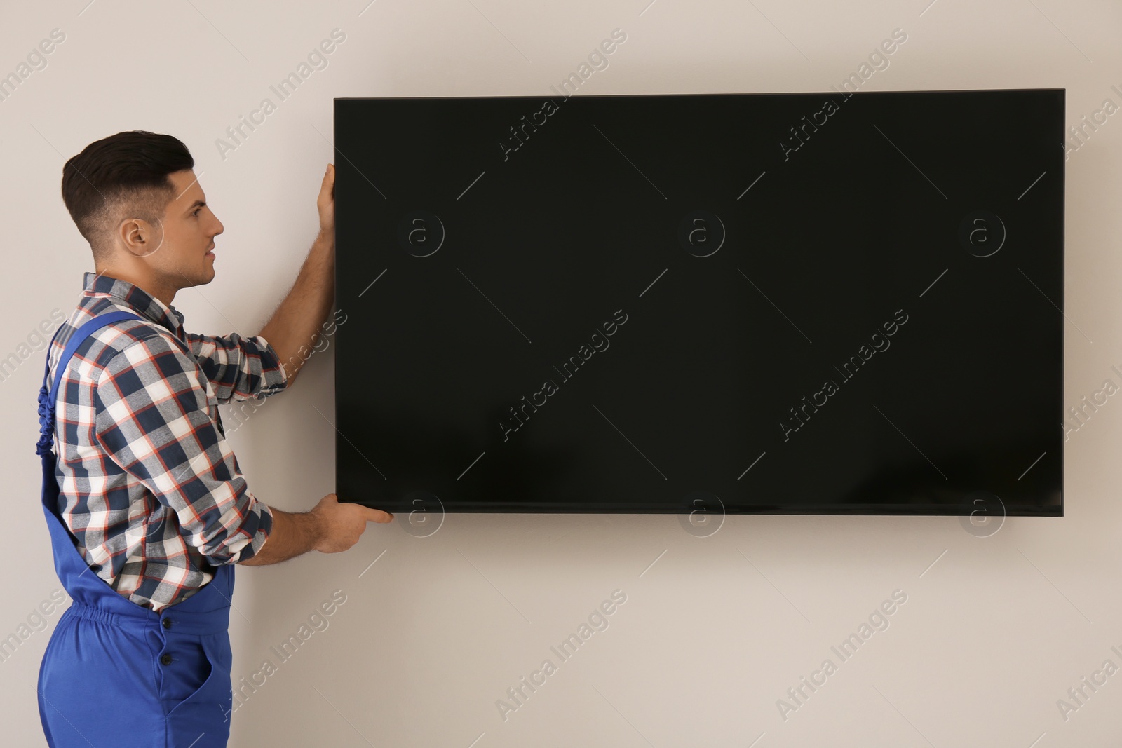 Photo of Professional technician installing modern flat screen TV on wall indoors