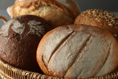 Photo of Wicker basket with different types of fresh bread against grey background, closeup