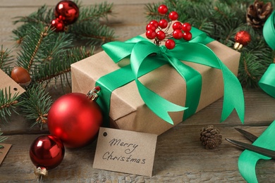 Photo of Christmas gift box with green bow and fir tree branches on wooden table