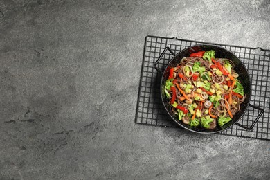 Stir fried noodles with mushrooms and vegetables in wok on grey table, top view. Space for text