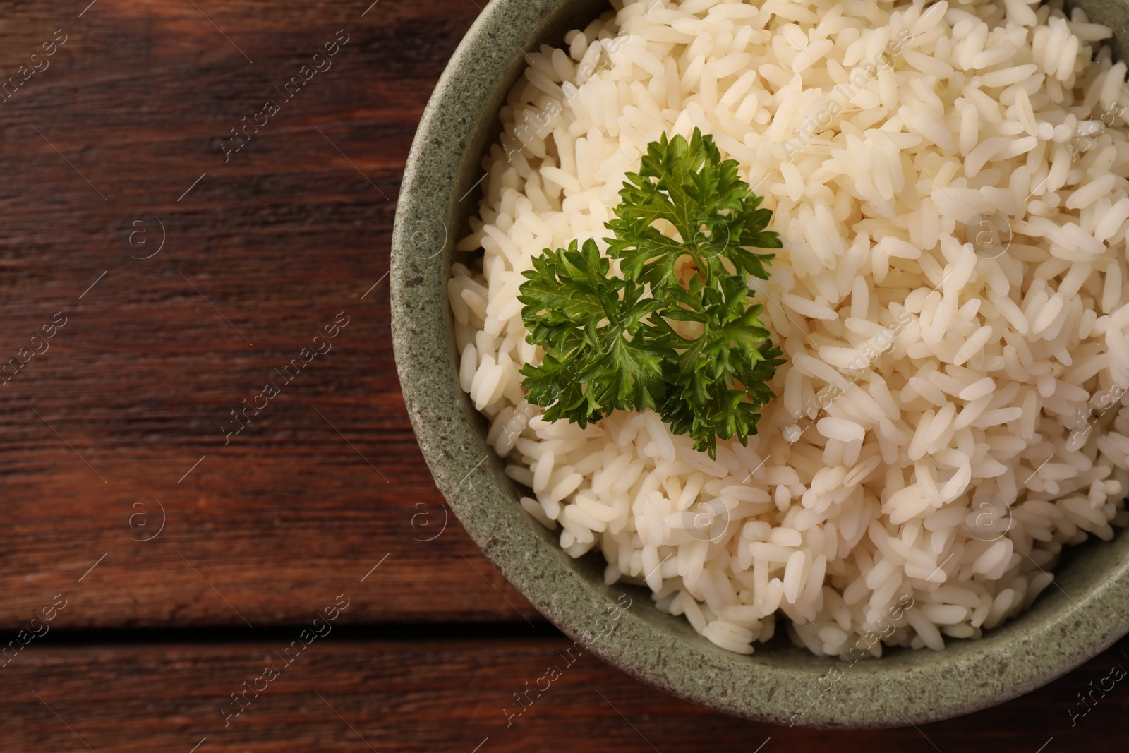 Photo of Delicious rice with parsley in bowl on wooden table, top view. Space for text