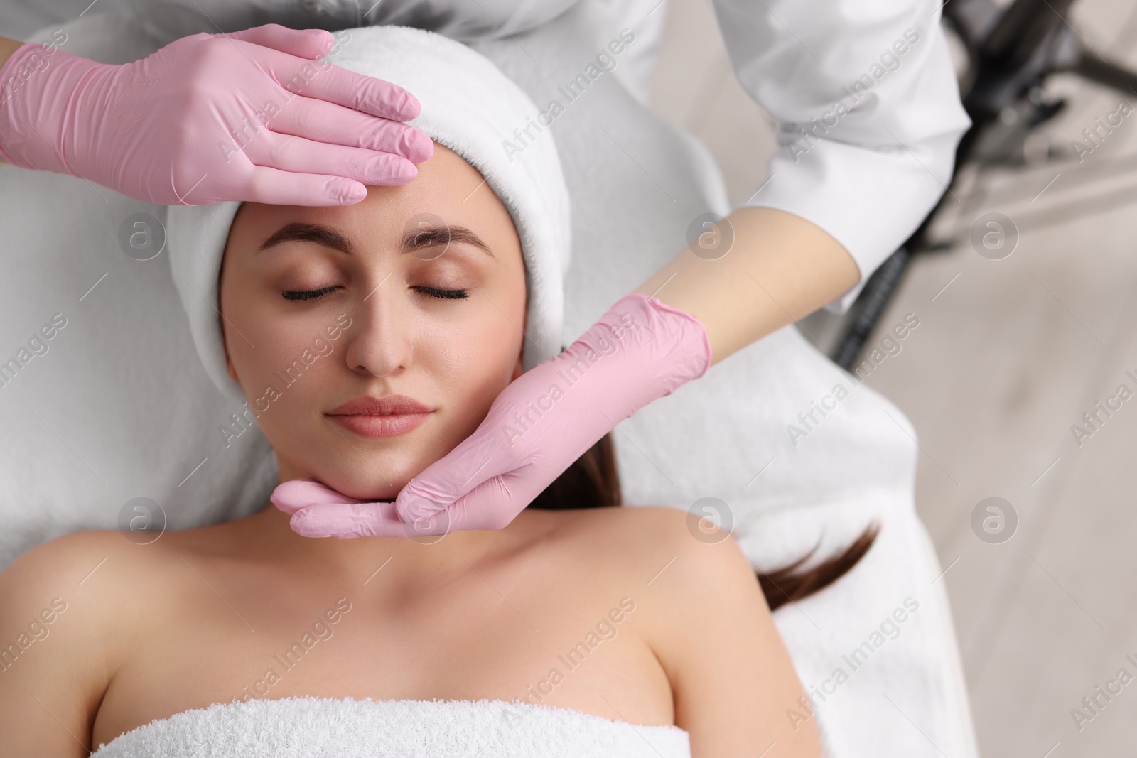 Photo of Cosmetologist making face massage to client in clinic, top view