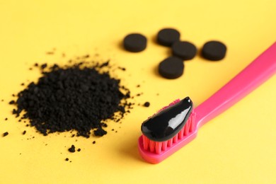 Photo of Brush with charcoal toothpaste, powder and tablets on yellow background