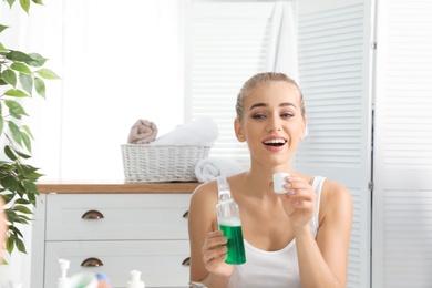 Photo of Woman holding bottle and cap with mouthwash in bathroom. Teeth care