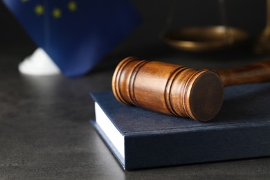 Wooden judge's gavel and book on grey table against European Union flag, closeup. Space for text