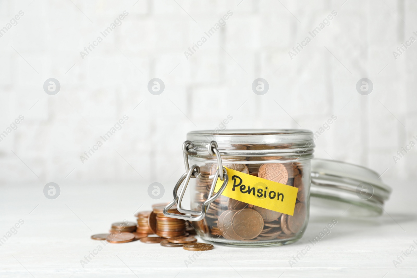 Photo of Coins in glass jar with label "PENSION" on table against light wall. Space for text