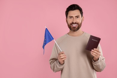 Photo of Immigration. Happy man with passport and flag of European Union on pink background, space for text