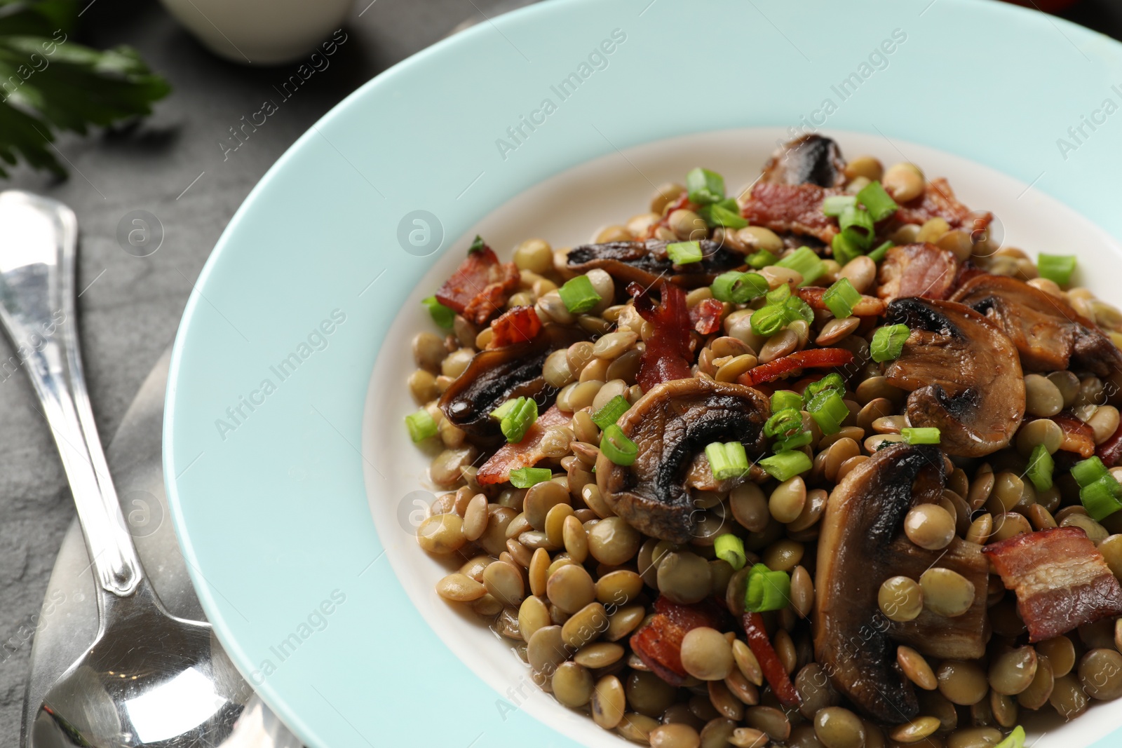 Photo of Delicious lentils with mushrooms, bacon and green onion on table, closeup