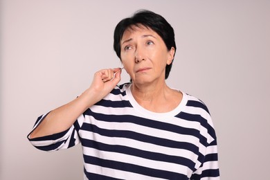 Photo of Senior woman cleaning ear with cotton swab on light grey background