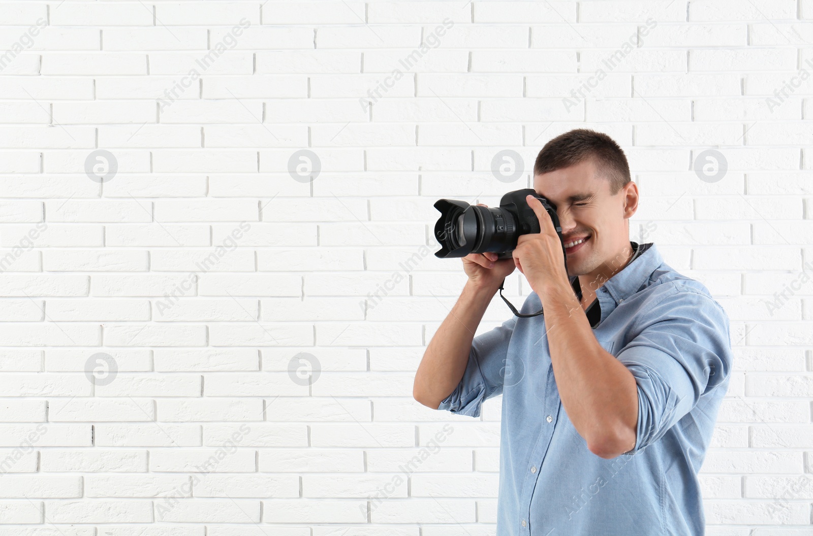 Photo of Young professional photographer taking picture near brick wall. Space for text