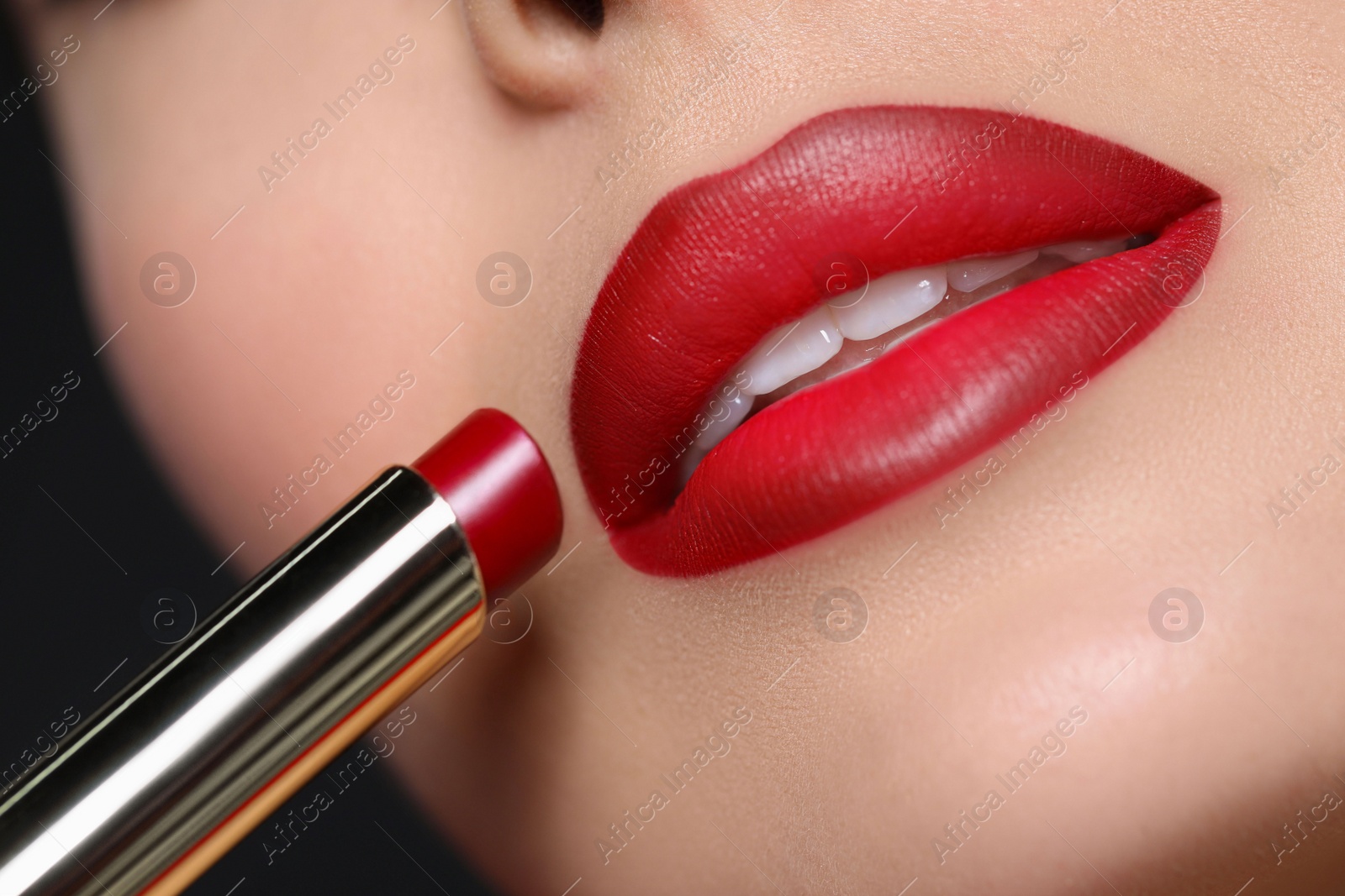 Photo of Young woman with beautiful makeup holding red lipstick on black background, closeup