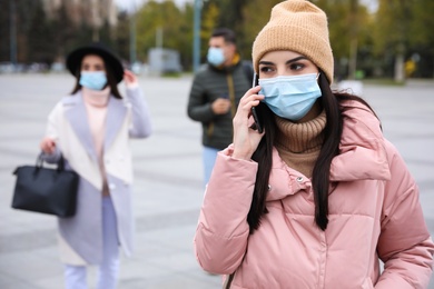 Young woman in medical face mask talking on phone while walking outdoors. Personal protection during COVID-19 pandemic