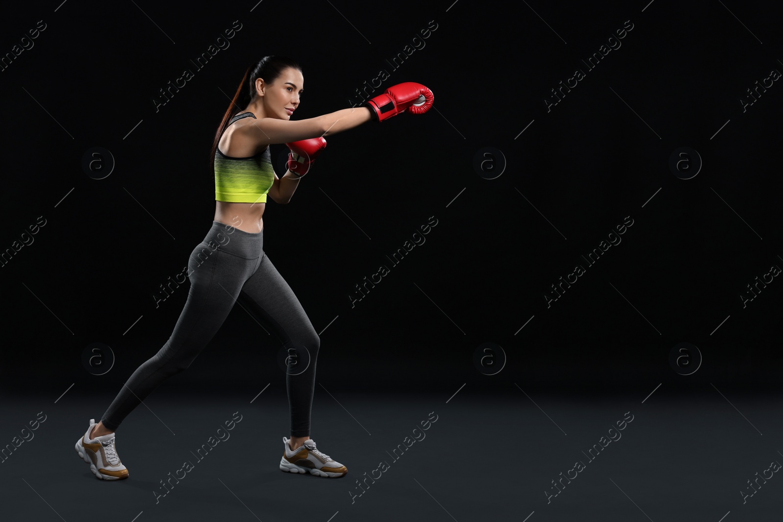 Photo of Beautiful woman in boxing gloves training on black background. Space for text