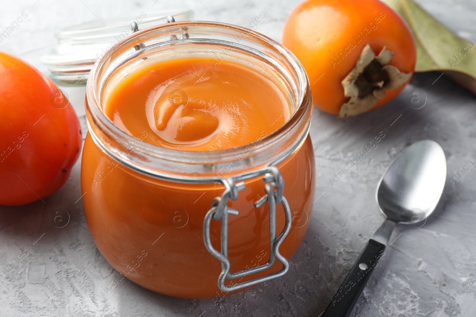 Photo of Delicious persimmon jam and fresh fruits on grey table, closeup