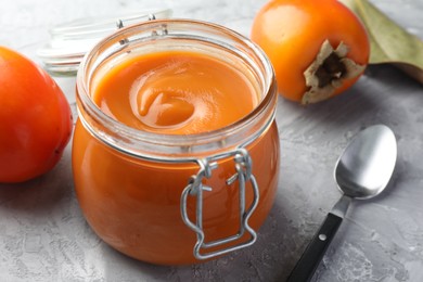 Photo of Delicious persimmon jam and fresh fruits on grey table, closeup