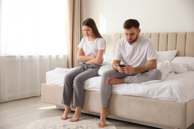 Photo of Man with smartphone ignoring his girlfriend at home. Relationship problems