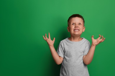 Photo of Angry little boy on green background, space for text. Aggressive behavior