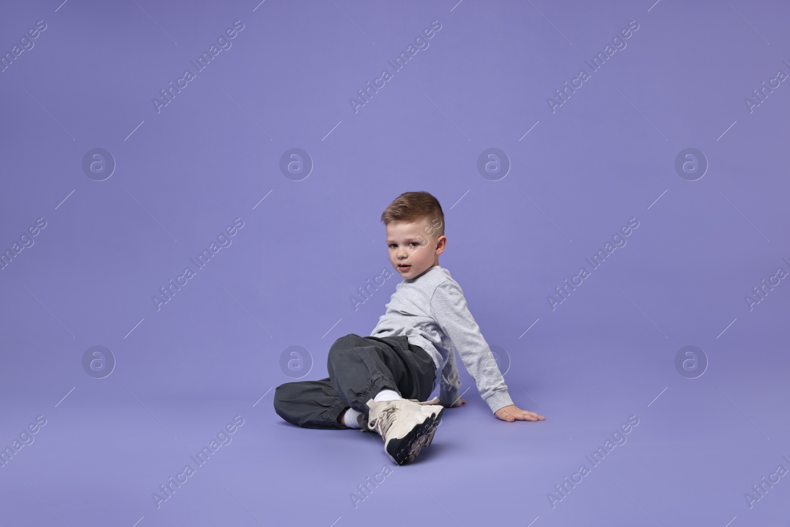 Photo of Happy little boy dancing on violet background