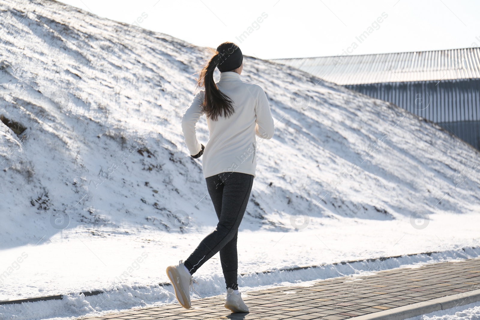 Photo of Woman running past snowy hill in winter, back view. Outdoors sports exercises