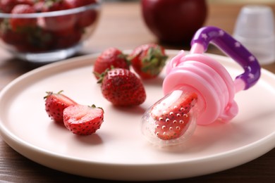 Photo of Plastic nibbler with fresh strawberries on plate, closeup. Baby feeder