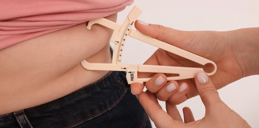 Image of Nutritionist measuring overweight woman's body fat layer with caliper on white background, closeup. Banner design