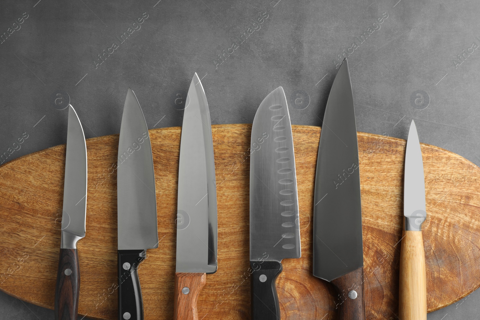 Photo of Many different knives and wooden board on grey textured table, flat lay