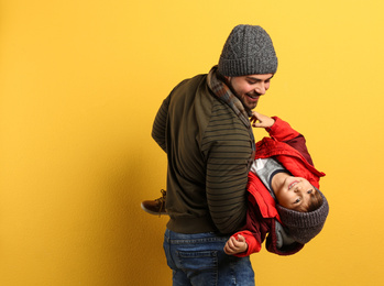 Happy father and son in warm clothes playing on yellow background, space for text. Winter vacation