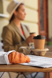 Woman with coffee in outdoor cafe, focus on croissant