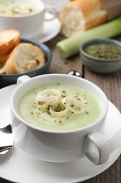 Delicious cream soup with leek and spices in bowl on wooden table, closeup