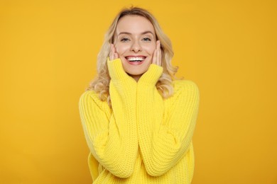 Happy woman in stylish warm sweater on orange background