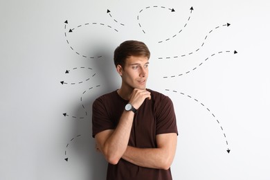 Image of Choice in profession or other areas of life, concept. Making decision, thoughtful young man surrounded by drawn arrows on light background