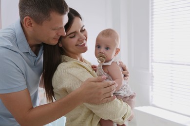 Photo of Happy couple and their cute little baby with pacifier at home