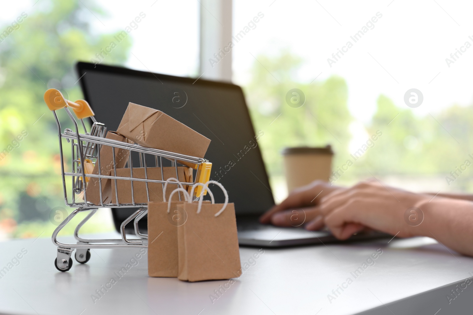 Photo of Internet shopping. Small cart with boxes and bags near woman using laptop indoors