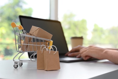 Photo of Internet shopping. Small cart with boxes and bags near woman using laptop indoors