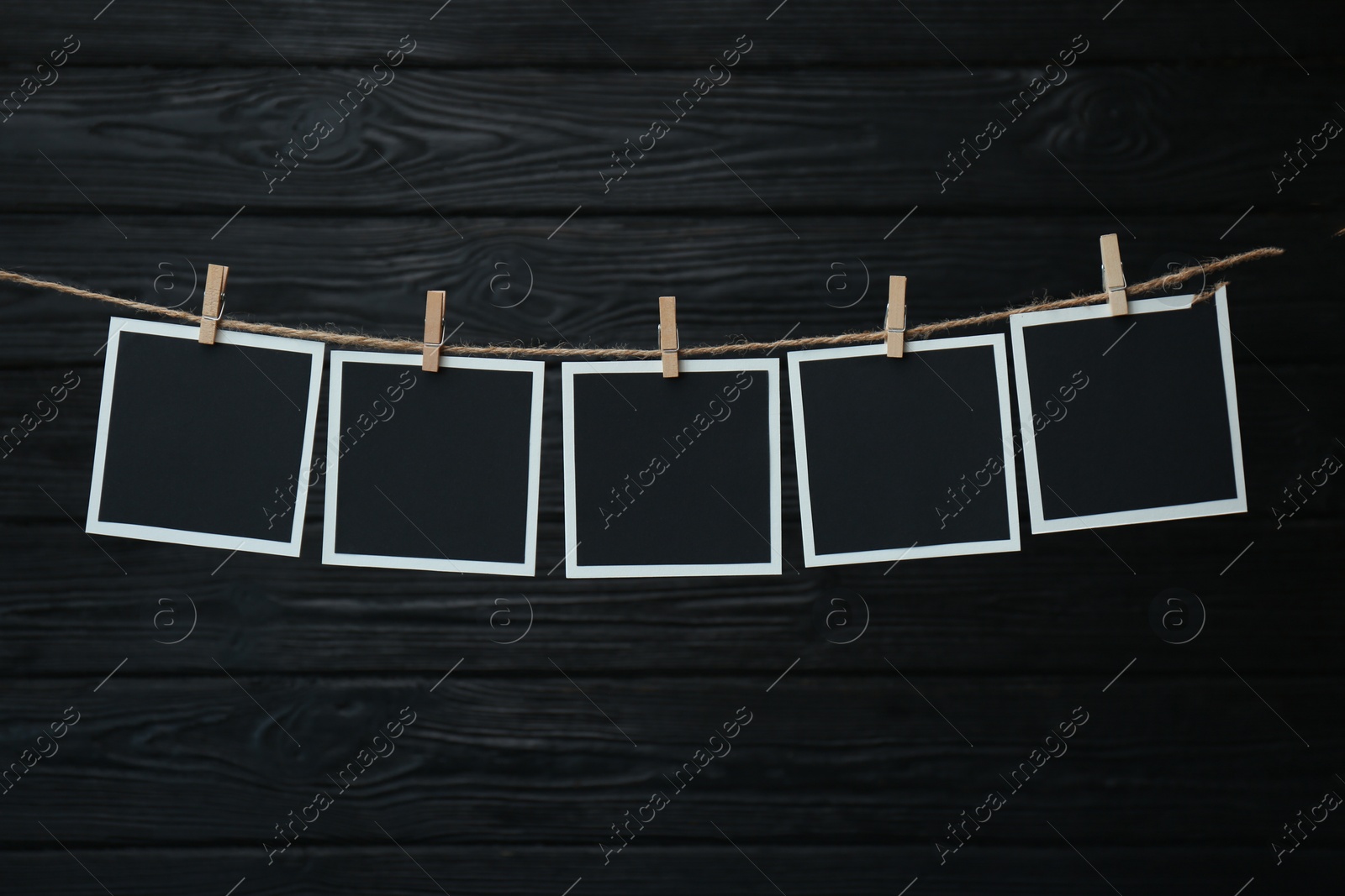 Photo of Clothespins with empty instant frames on twine against black wooden background. Space for text