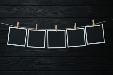 Photo of Clothespins with empty instant frames on twine against black wooden background. Space for text
