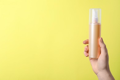 Photo of Woman holding spray bottle with hair thermal protection against pale yellow background, closeup. Space for text
