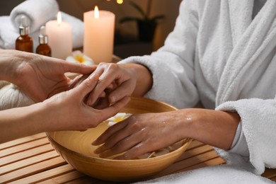 Woman receiving hand massage in spa salon, closeup. Bowl of water and flowers on wooden table