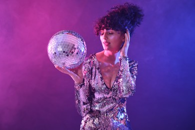 Photo of Beautiful young woman with disco ball posing on color background in neon lights