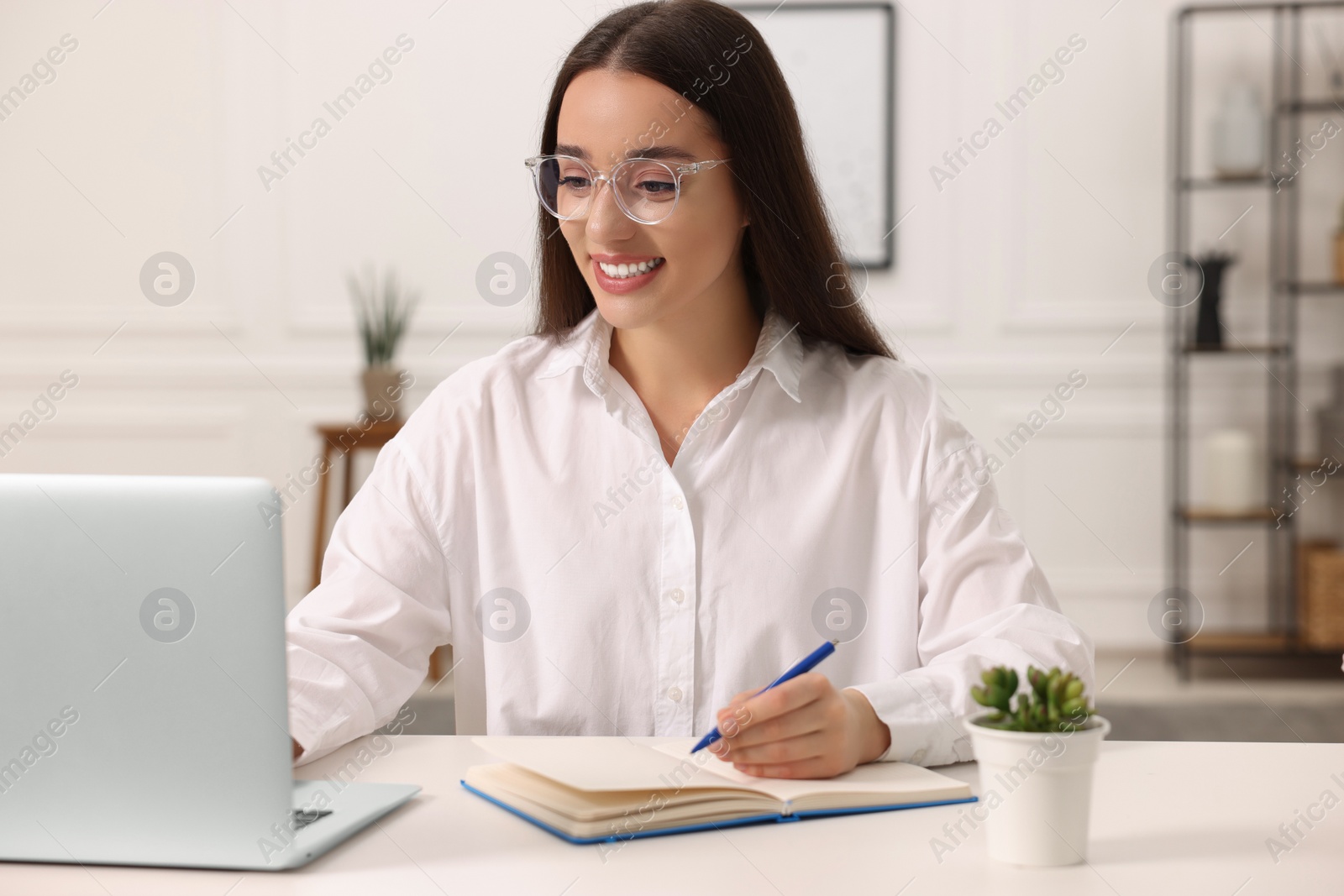 Photo of Young woman writing in notebook at white table indoors