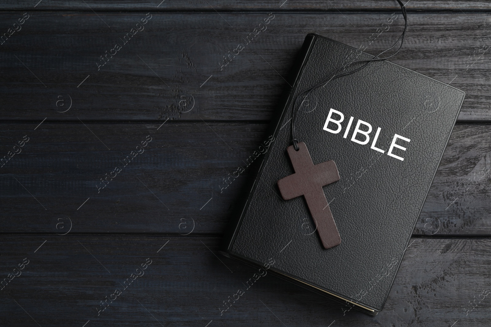 Photo of Christian cross and Bible on black wooden table, top view. Space for text