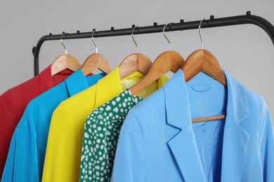 Rack with stylish women`s clothes on wooden hangers against light grey background, closeup