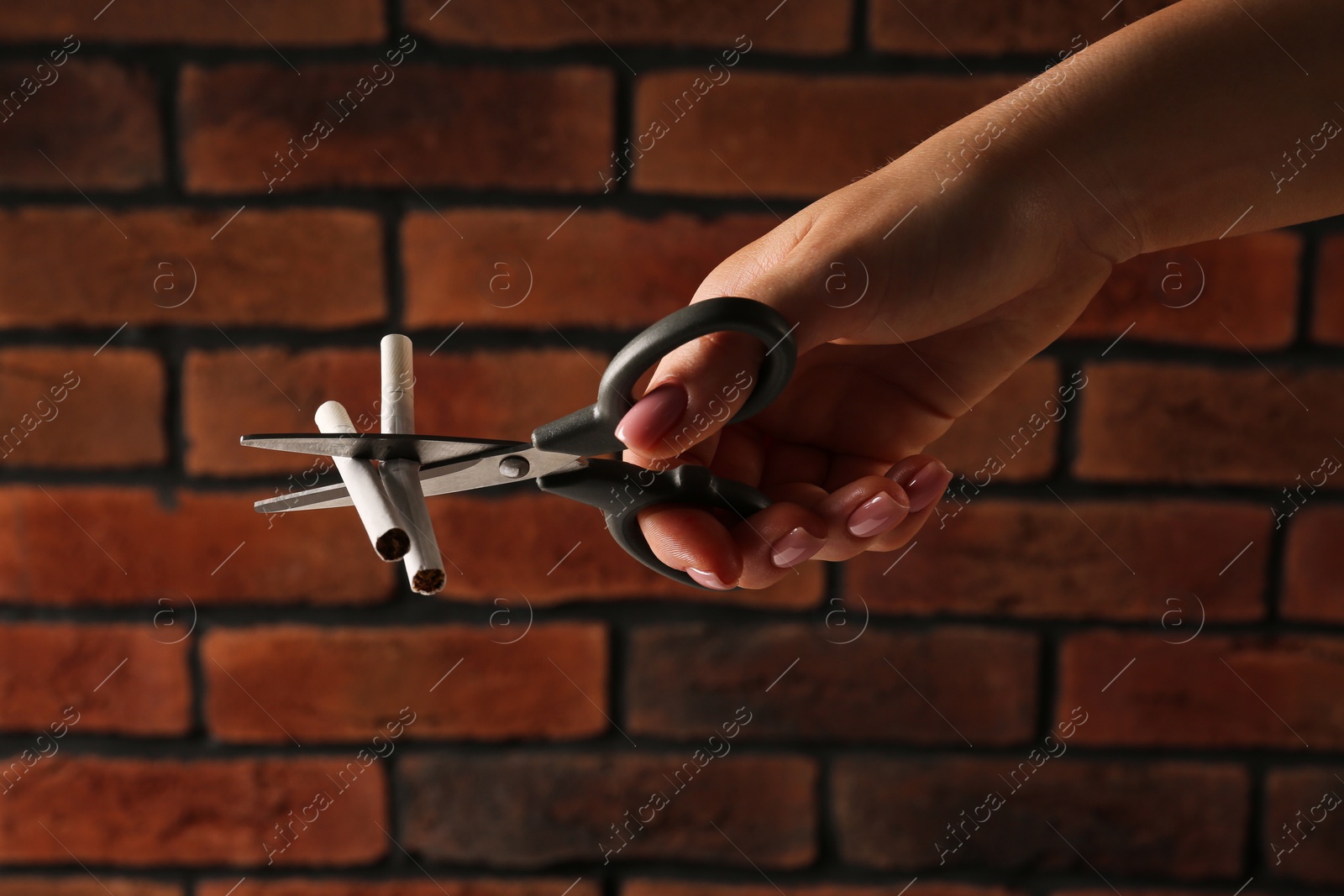 Photo of Woman cutting cigarettes with scissors near brick wall, closeup. No smoking concept