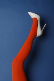 Photo of Woman wearing bright tights and high heel shoe on blue background, closeup