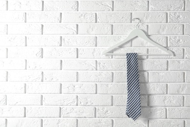 Photo of Tie on wooden hanger against brick wall. Space for text