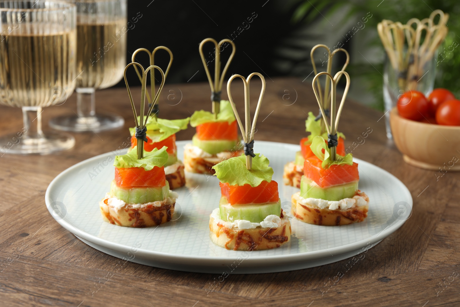 Photo of Tasty canapes with salmon, cucumber, bread and cream cheese on wooden table
