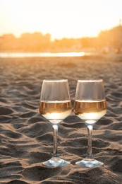 Photo of Glasses of tasty wine on sand near sea