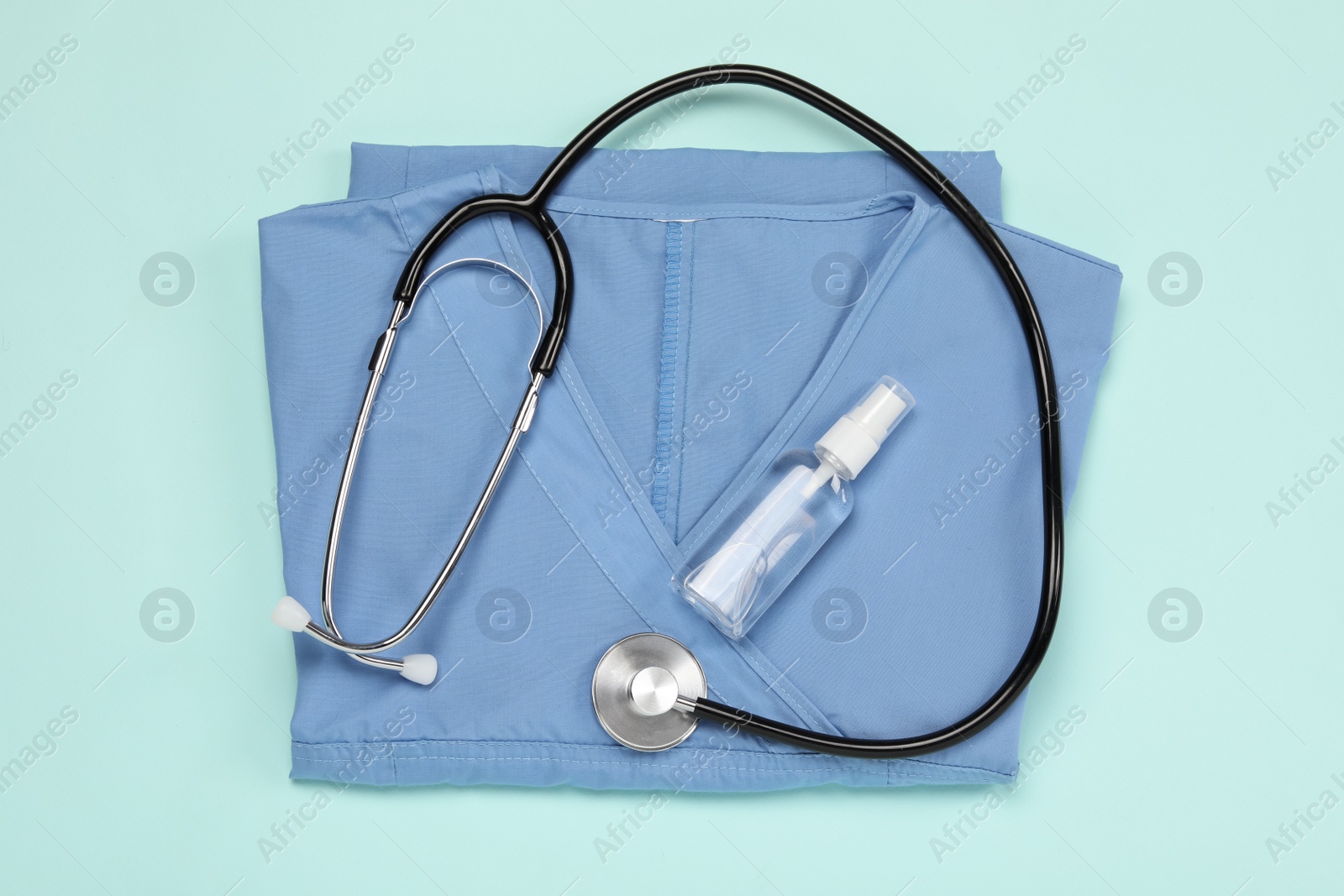 Photo of Medical uniform, stethoscope and antiseptic on light blue background, flat lay