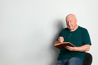 Photo of Portrait of senior man with glasses reading book on light background. Space for text