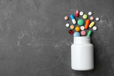 Bottle with different pills on grey background, flat lay. Space for text